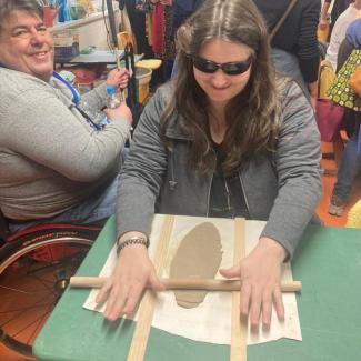 Blinde Frau beim Ausrollen von Ton mit hilfe eines Stabes und  zwei Holzauflagen