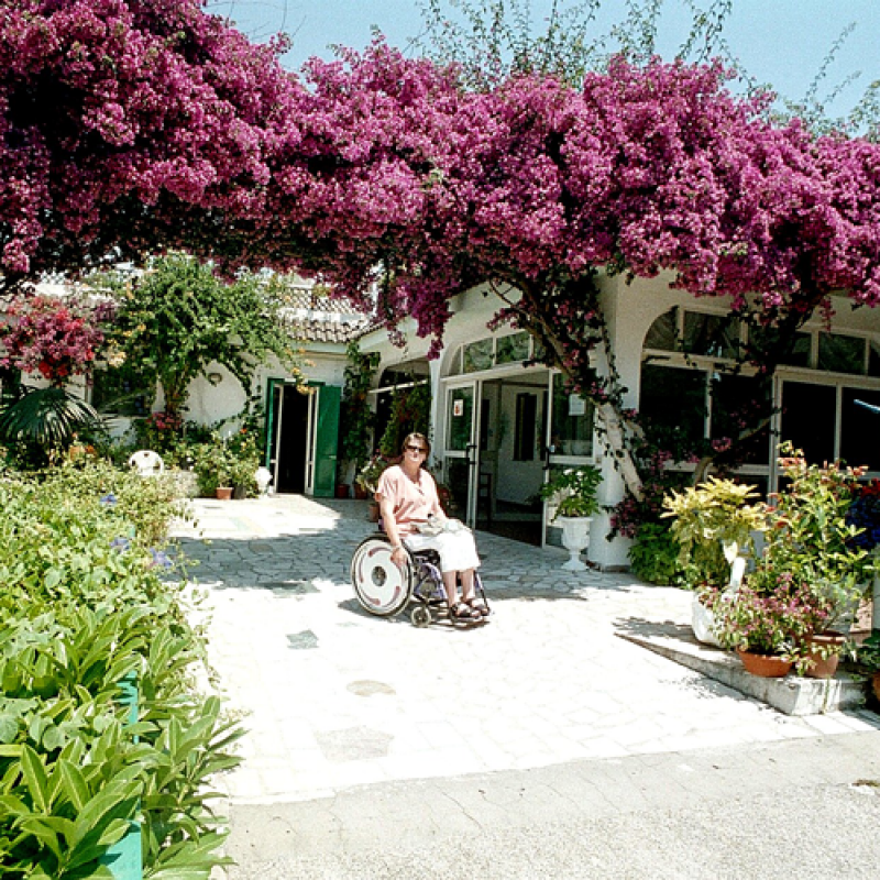 Bild zeigt: Rollstuhlfahrerin in einem wundervoll blühenden ebenerdigen Eingangsbereich