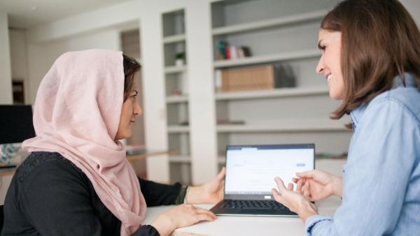 Bild zeigt 2 Frauen eine erklärt einer Frau mit Kopftuch etwas am Laptop