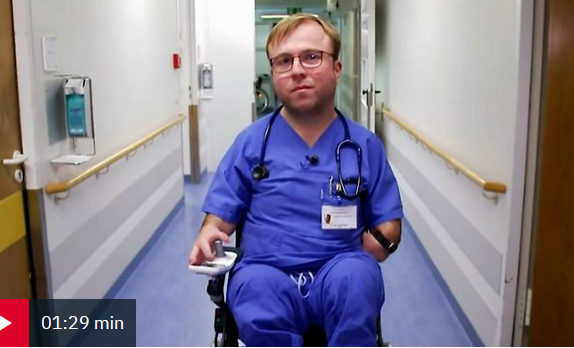Bild zeigt mann in einem Rollstuhl, er trägt blaue Klinikkleidung und ein Stethoskop