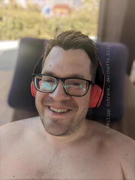 Philipp liegt entspannt auf einem Liegestuhl mit Kopfhörern auf und grinst in die Kamera.