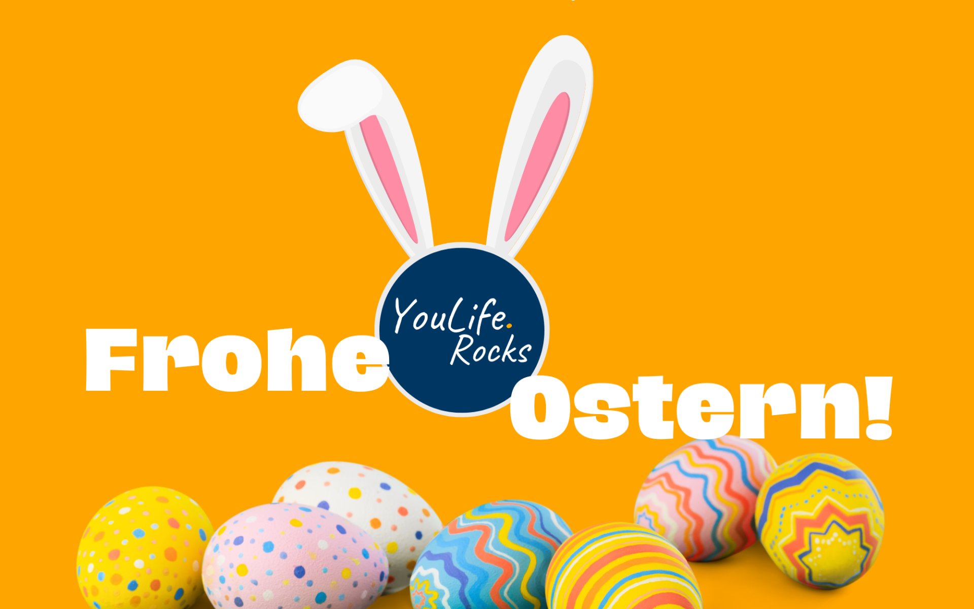 Der Schriftzug "Frohe Ostern!" in fetten weißen Buchtaben. Zwischen den Wörtern ist das YouLife.Rocks Logo eingebettet mit aufgesetzten rosa Hasenohren. Im Vordergrund ein Haufen an bunten Ostereiern in 3D-Optik