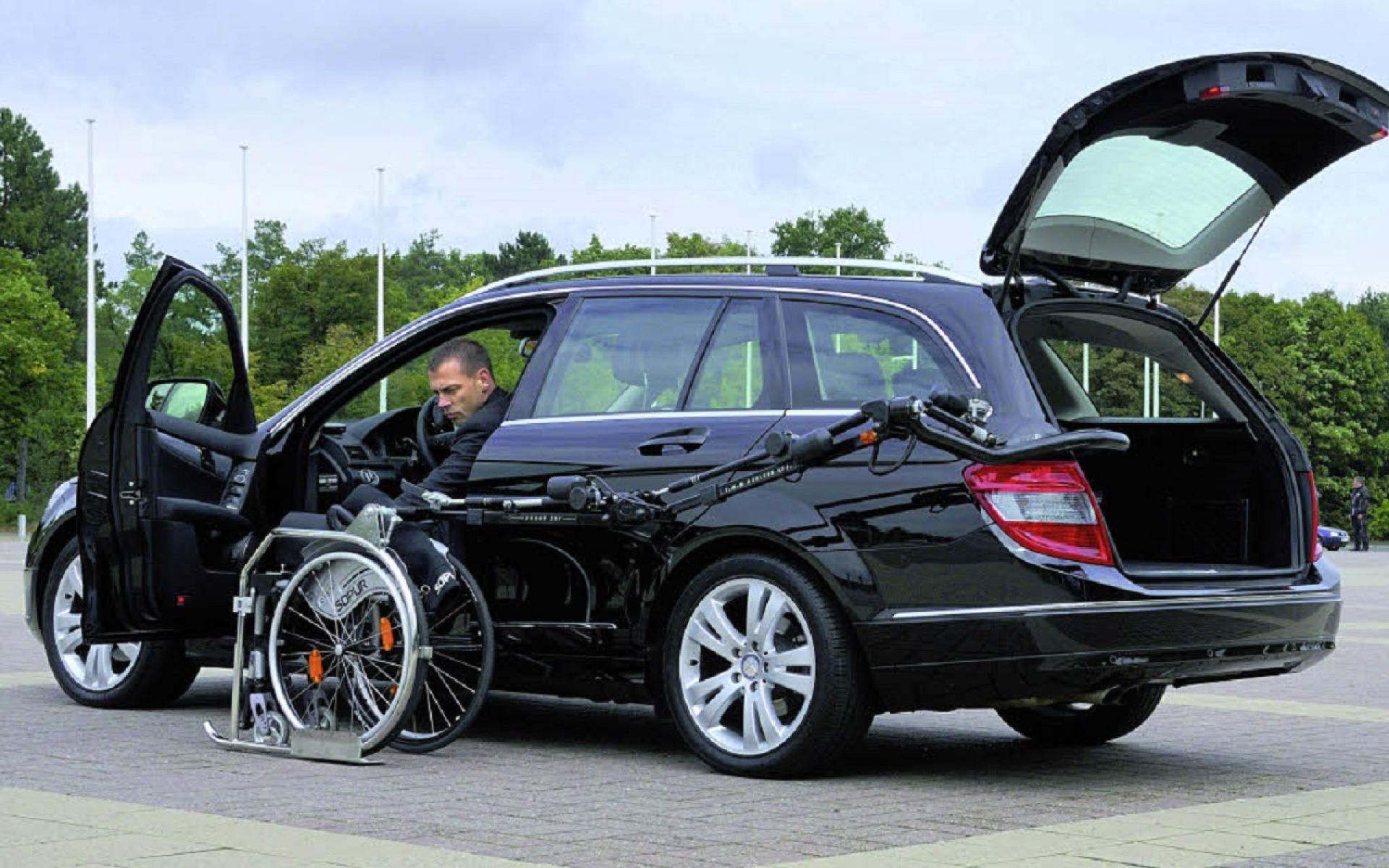 Mercedes Kombi mit Umbau für Rollstuhlfahrer ein Greifarm bringt den Rollstuhl vom Kofferraum zur Fahrertüre, wo ein Mann auf dem Fahrersitz ist