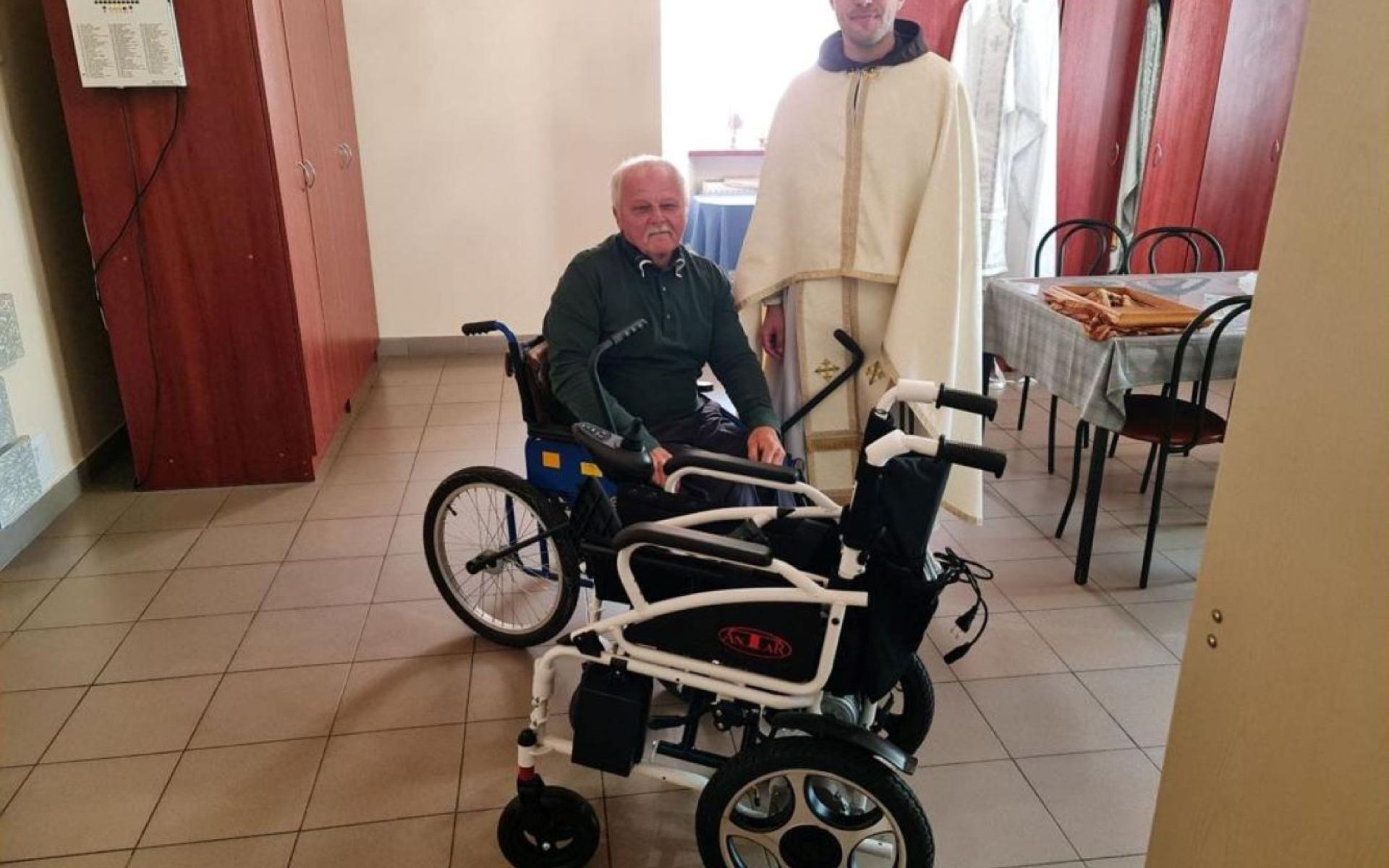 Bild Zeigt einen Mönch des Ordens, einen Betroffenen im Rollstuhl, bei der Übergabe des neuen E-Rollstuhl