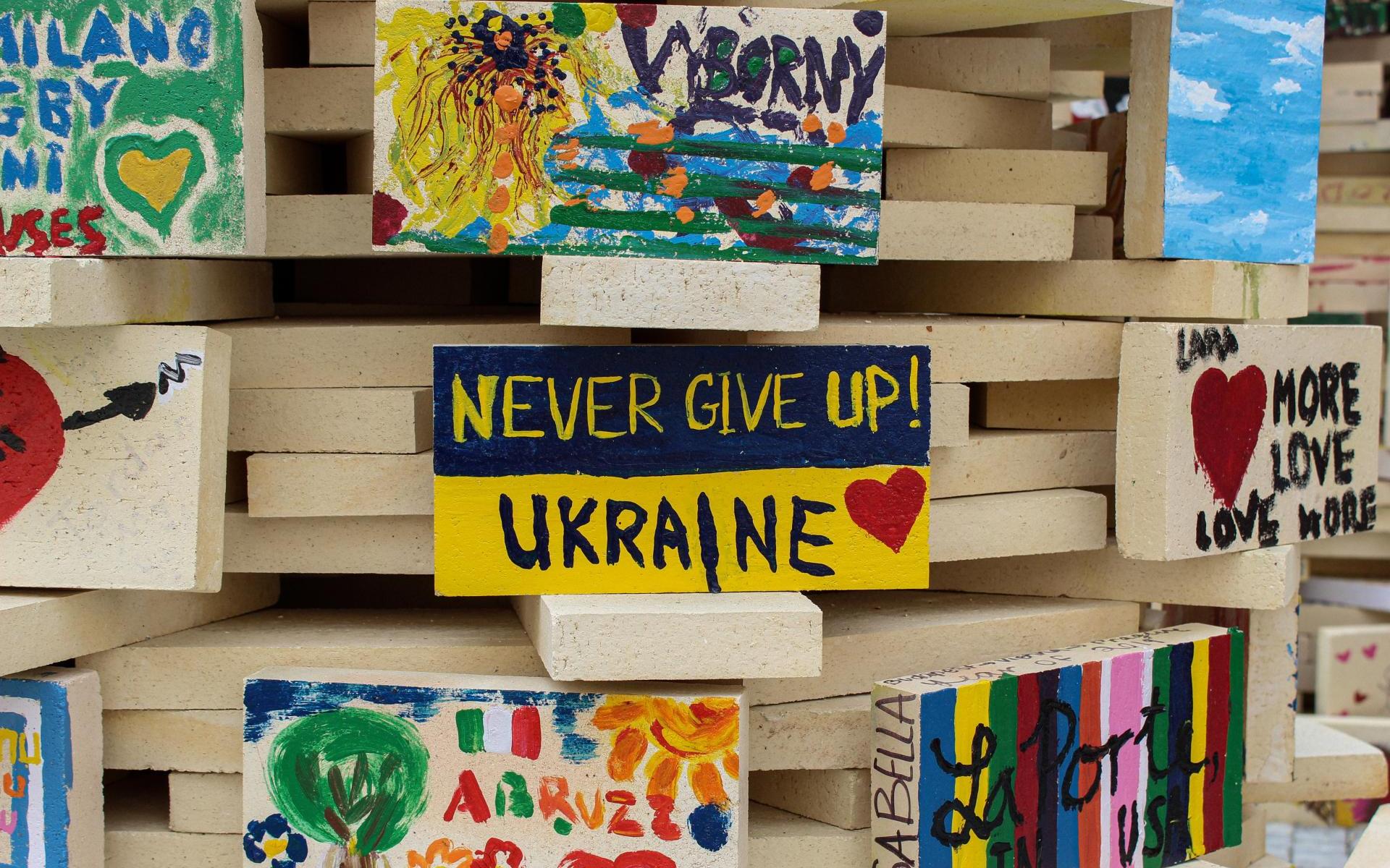 Bemalte Holzbretter gestapelt mit Botschaften wie "Never give up Ukraine"