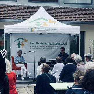 Blick auf die Bühne mit 2 Pesonen, eine Frau liest aus einem Buch, eim Mann begleitet sie dabei auf einem E-Piano