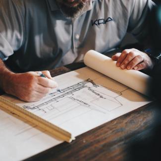 Bild zeigt Mann der einen Bauplan mit dem Bleistift zeichnet