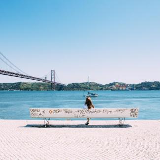 Frau auf einer Bank mit Blick auf einen Brücke in Lisbon Portugal