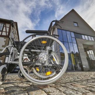 Bild zeigt Rollstuhl auf Kopfsteinpflaster vor dem Rathausneubau