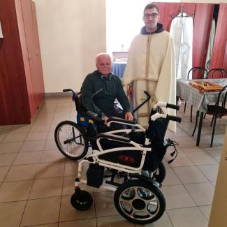 Bild Zeigt einen Mönch des Ordens, einen Betroffenen im Rollstuhl, bei der Übergabe des neuen E-Rollstuhl