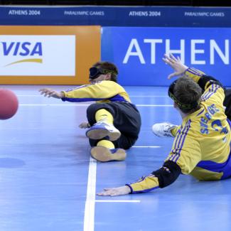 Bild zeigt eine Gruppe von Spieler beim Goball - ein Spiel für Blinde Menschen und alle Anderen. Die Spieler rutsche auf dem Boden mit Augenbinden und spielen mit dem Ball.