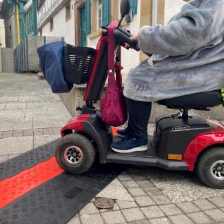 Eine Frau Befährt eine mit einem E-Scooter eine flache Kabelbrücke für Rollstühle