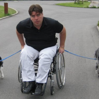 Rollstuhlfahrer der links und rechts einen Hund an der Leine hält