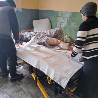 Bild zeigt Patient der von einem Bett in einem ärmlichen Zuhause auf eine Krankenliege umgebettet wird