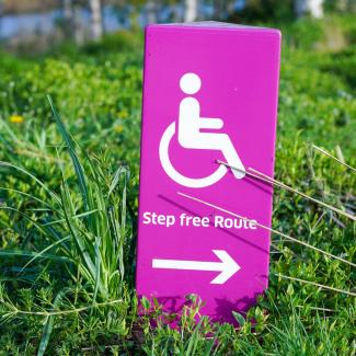 Wegweiser-Schild mit der englischen Aufschrift "Step free route" und einem Rollstuhlsymbol.